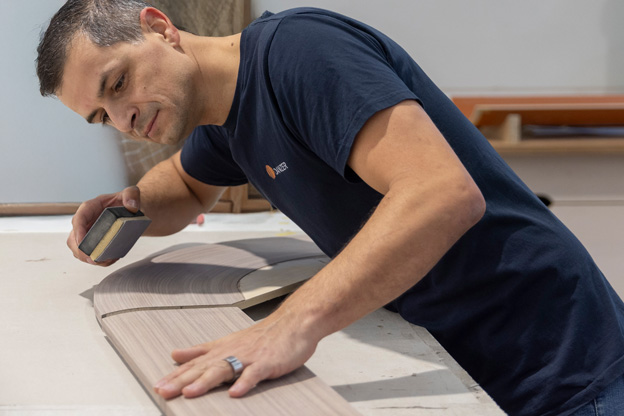 A skilled employee carefully sanding a curved wooden component at a workbench, representing Danzer's diverse and expert workforce.