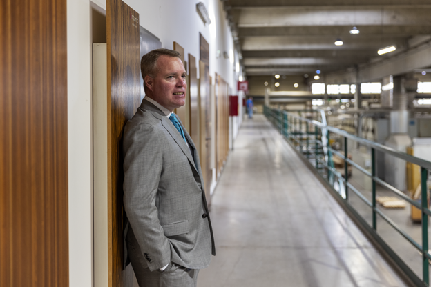 Hans-Joachim Danzer leaning against a wood-paneled wall overlooking a modern production facility walkway.